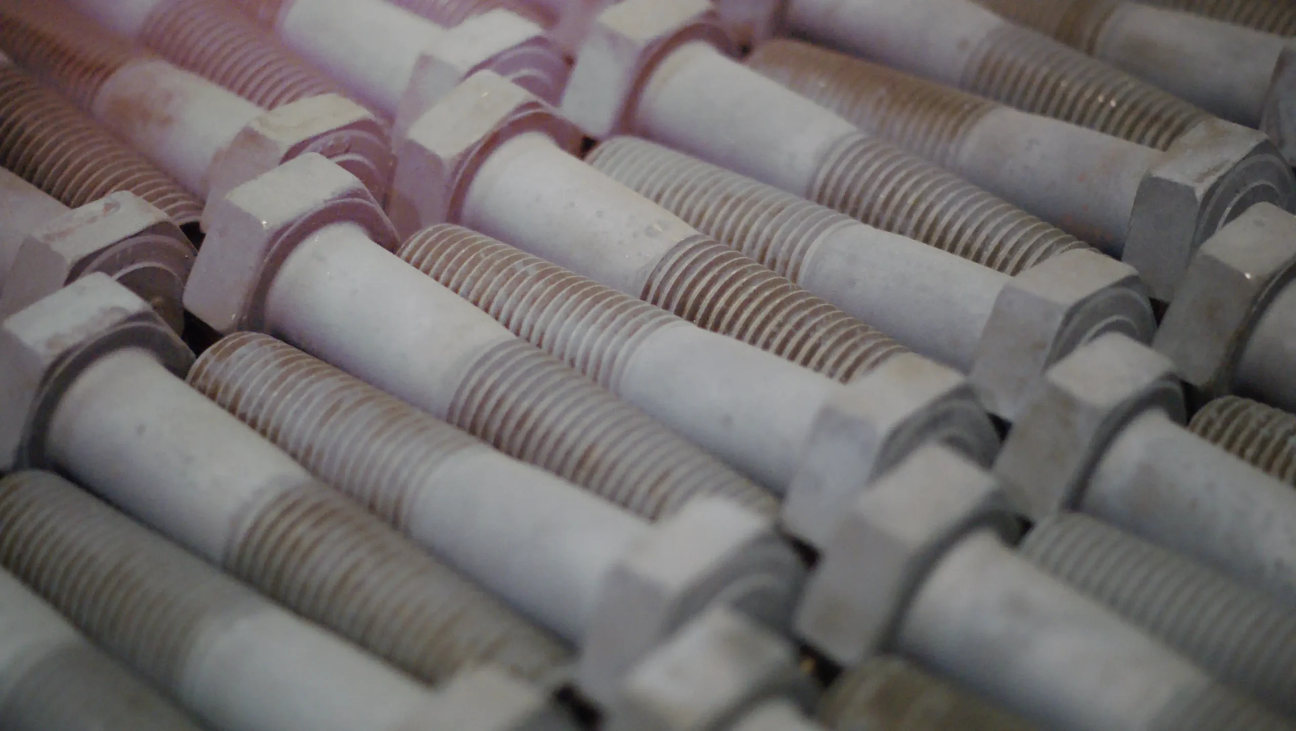 Close-up of rows of threaded metal bolts with hexagonal heads lined up.