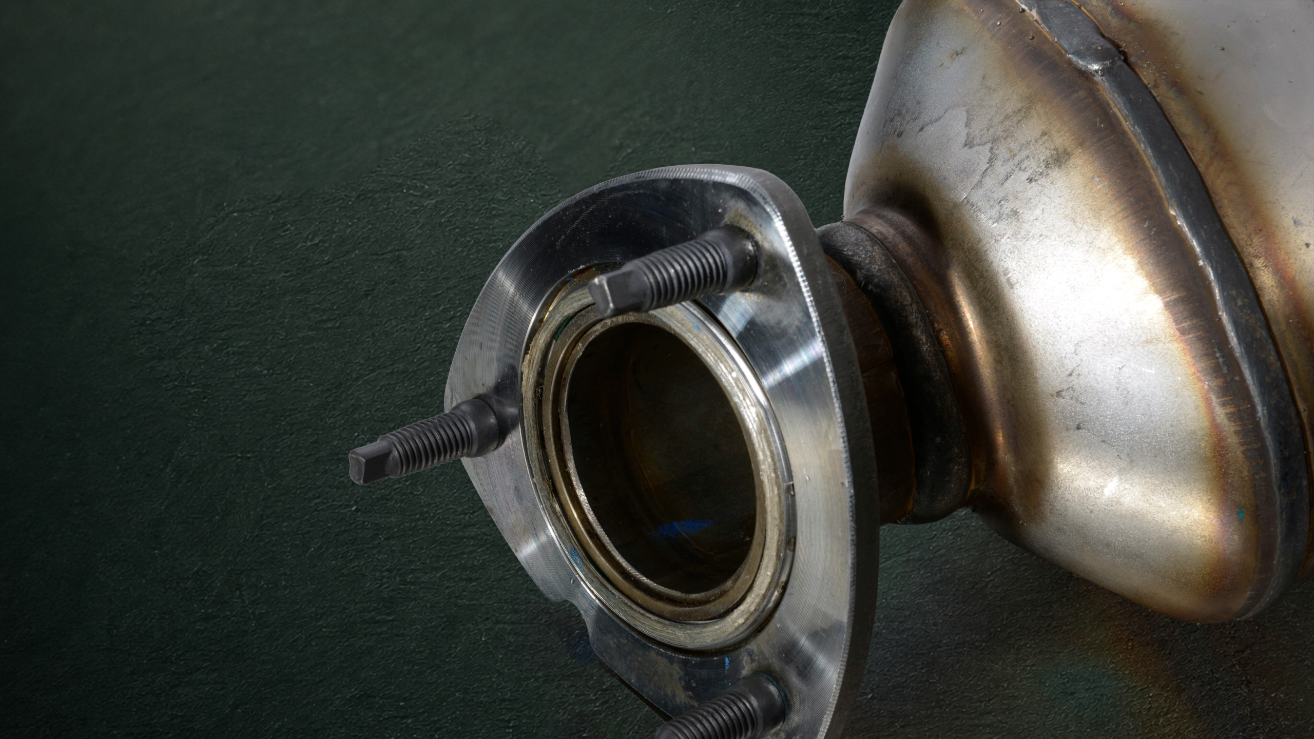 Close-up of a metal wheel hub flange with four bolt studs against a dark textured background.